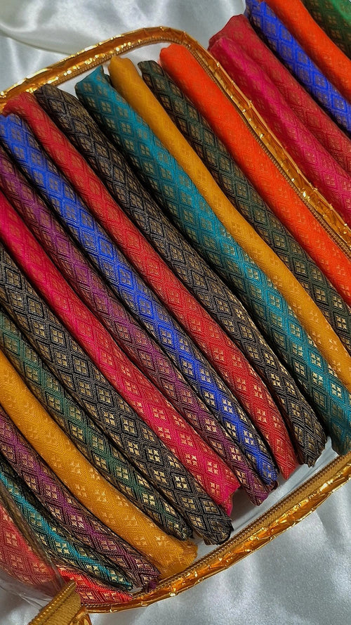 Multiple Banarasi silk blouse pieces rolled and displayed in a gold-trimmed box