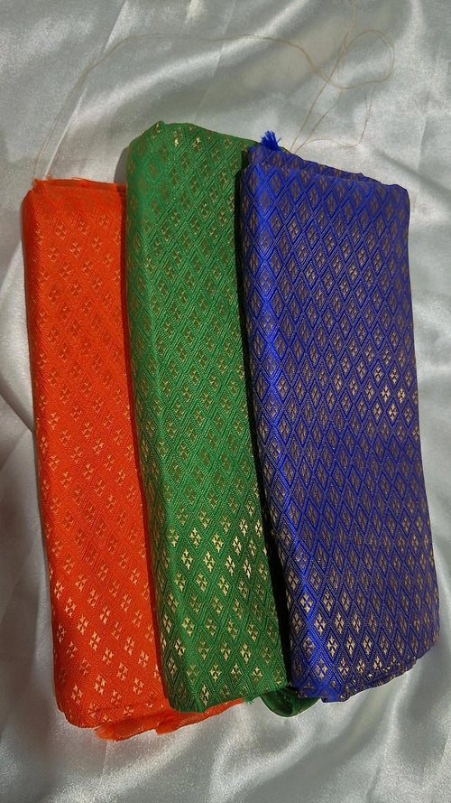 Three Banarasi silk blouse pieces in orange, green and blue folded on white satin