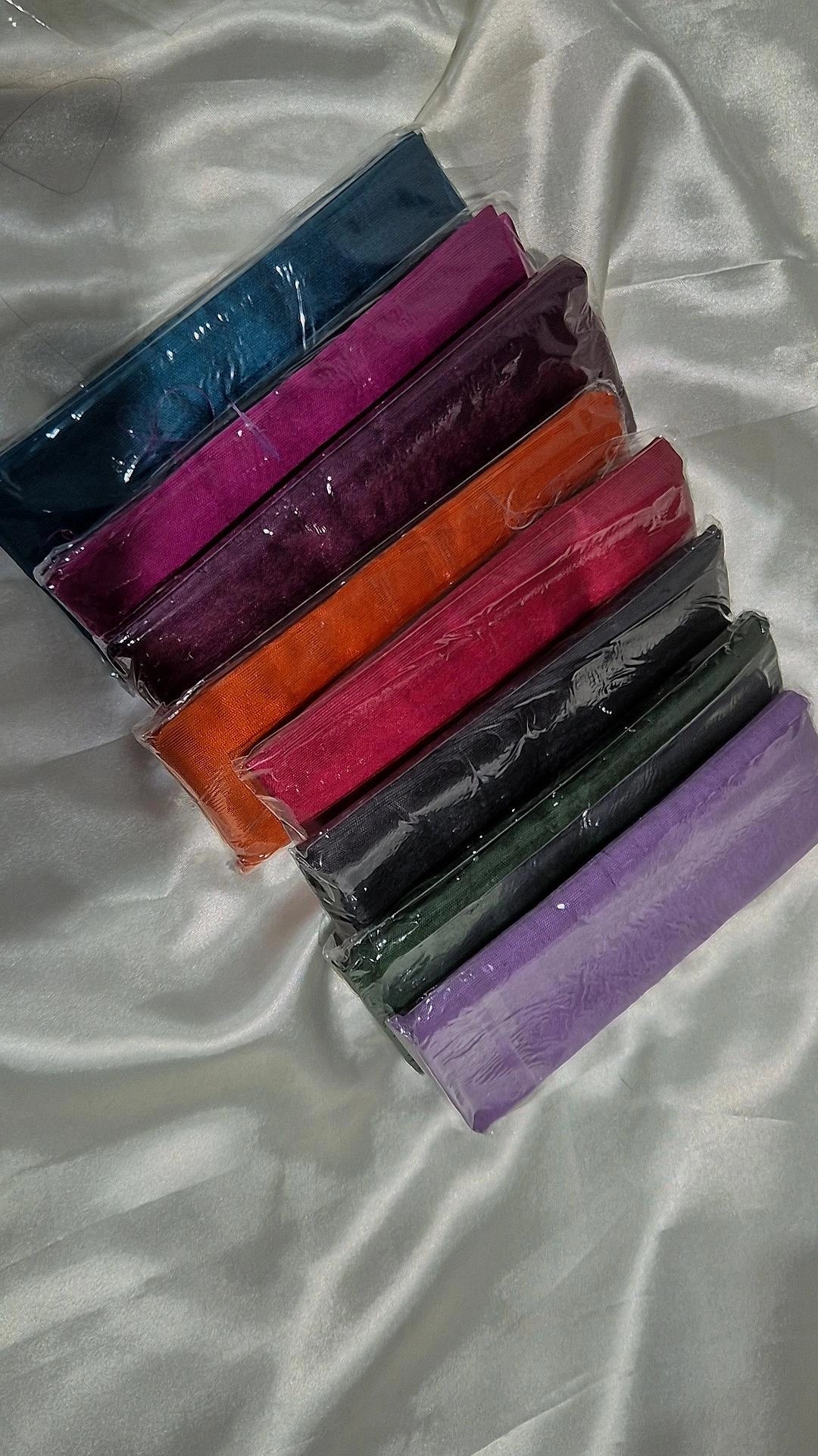 Raw silk blouse pieces in vibrant colours individually wrapped in clear sleeves on white satin