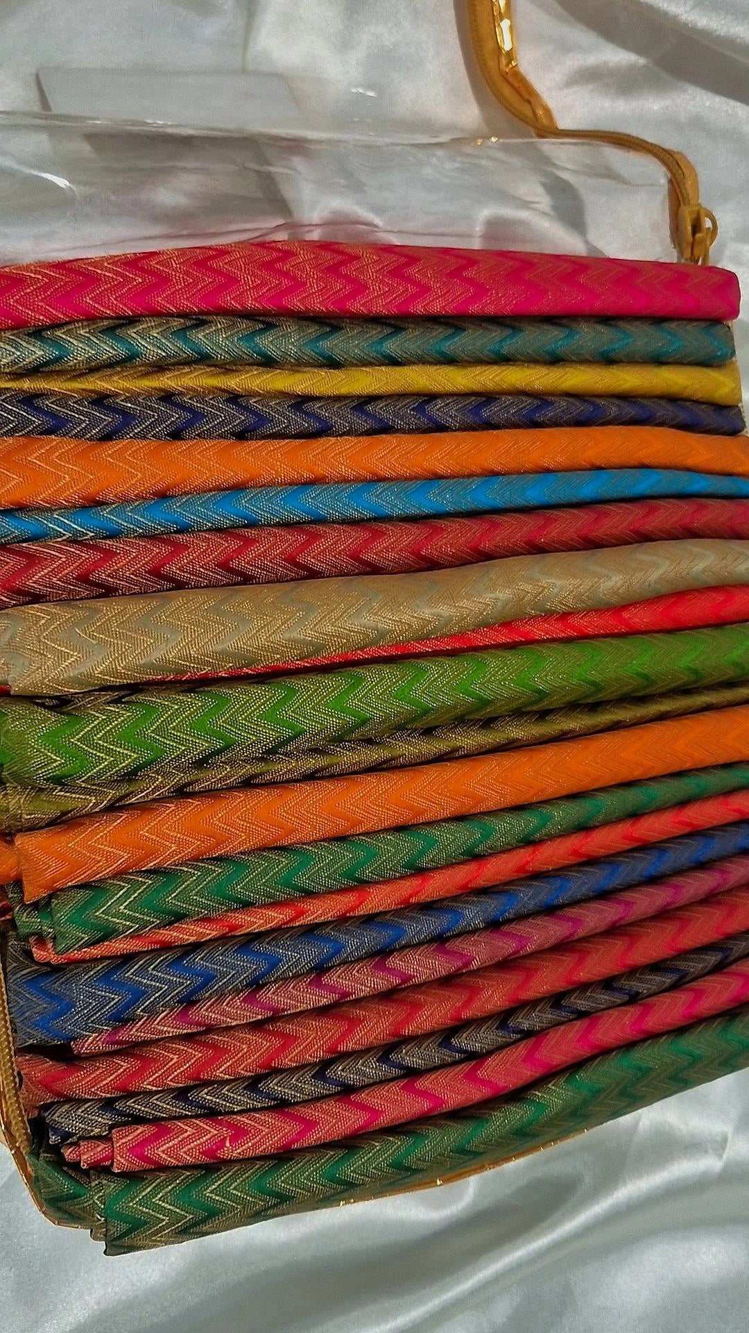 Multiple Banarasi silk chevron weave blouse pieces in vibrant colours stacked in a gold-trimmed box
