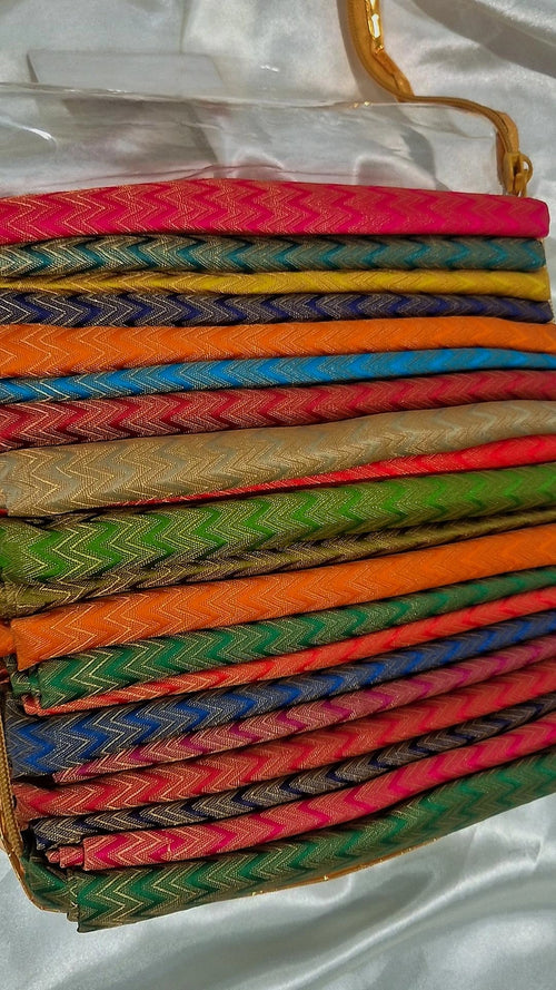 Multiple Banarasi silk chevron weave blouse pieces in vibrant colours stacked in a gold-trimmed box