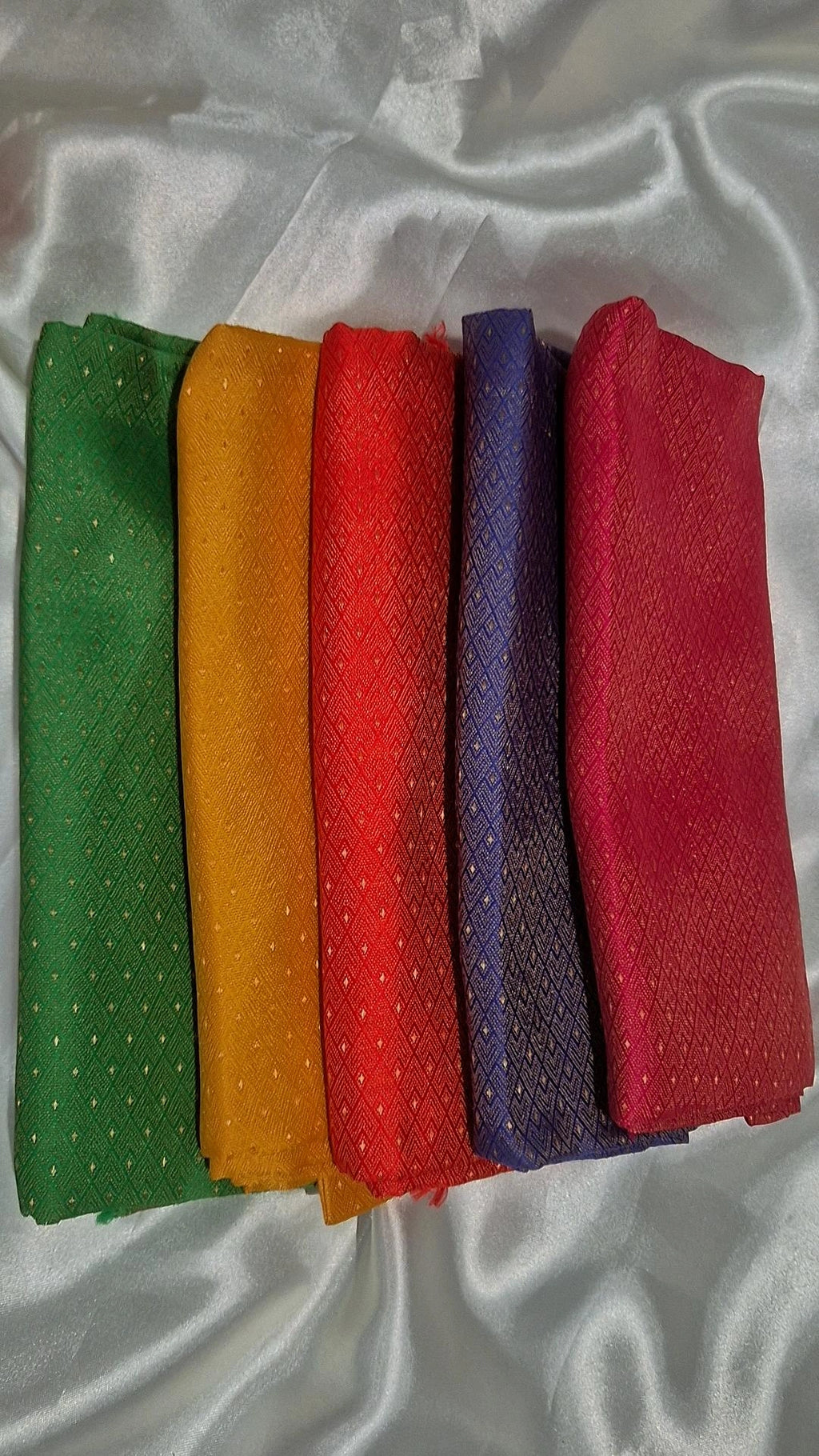 Five Banarasi silk blouse pieces in green, mustard, red, purple and pink fanned out on white satin
