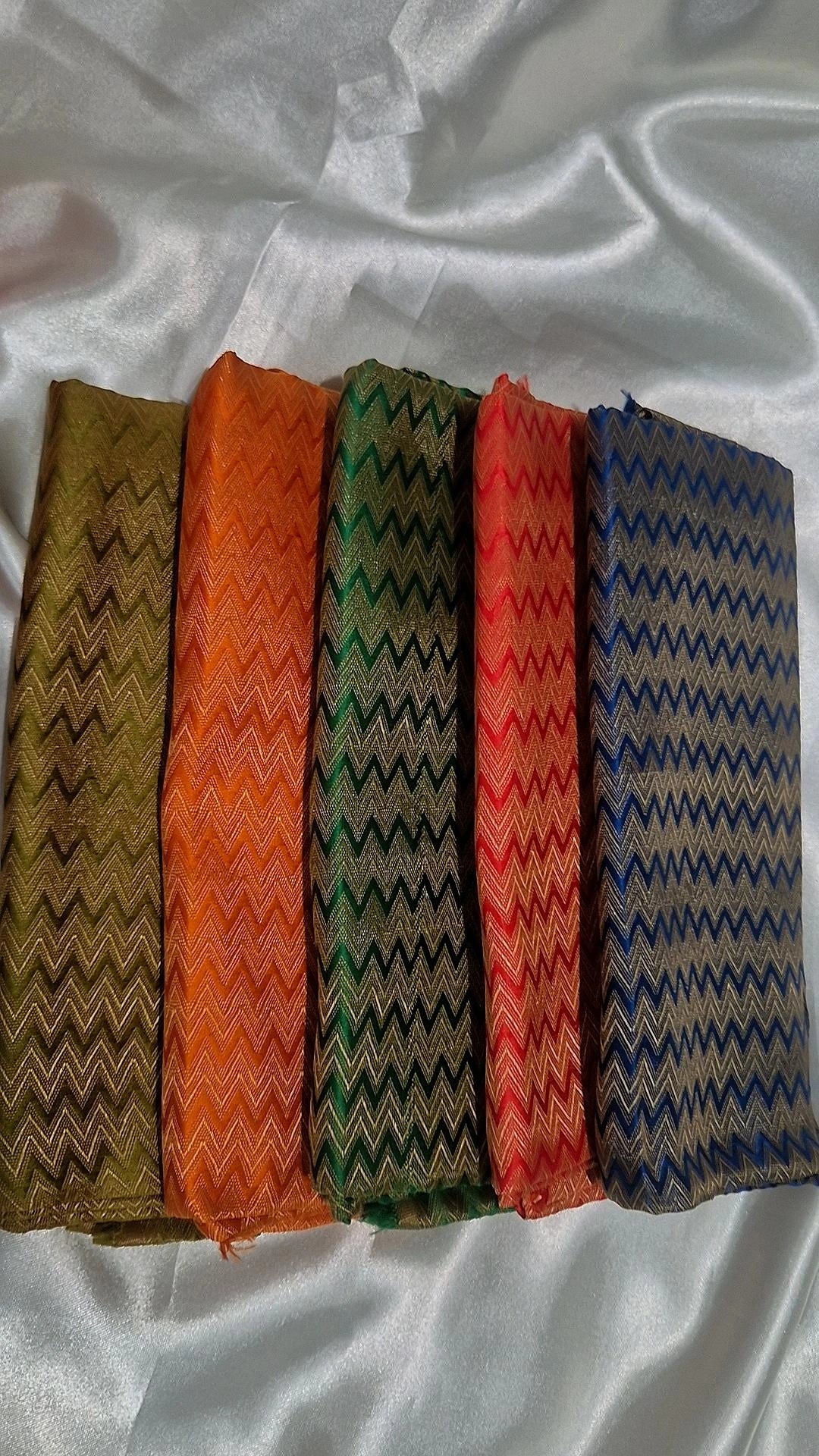 Five Banarasi silk chevron weave blouse pieces in olive, orange, green, red and blue fanned out on white satin