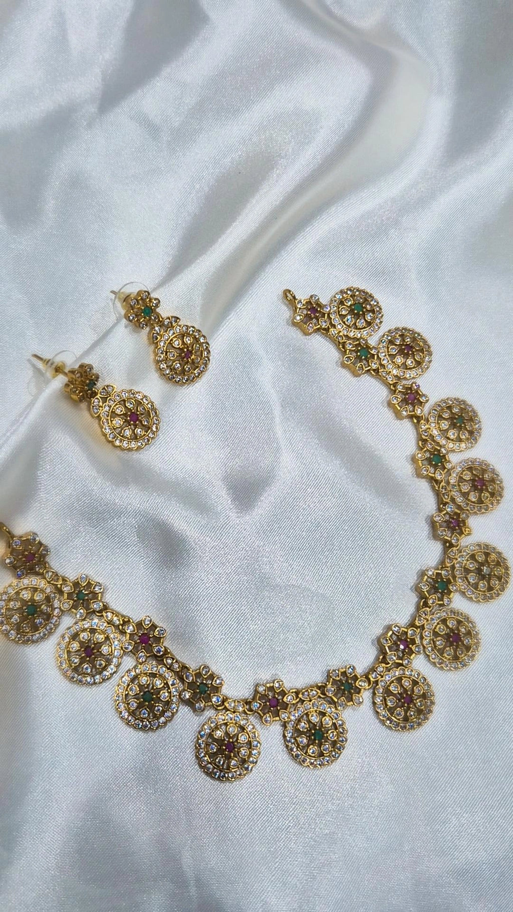 Gold-tone round motif kundan necklace and earring set laid on white fabric