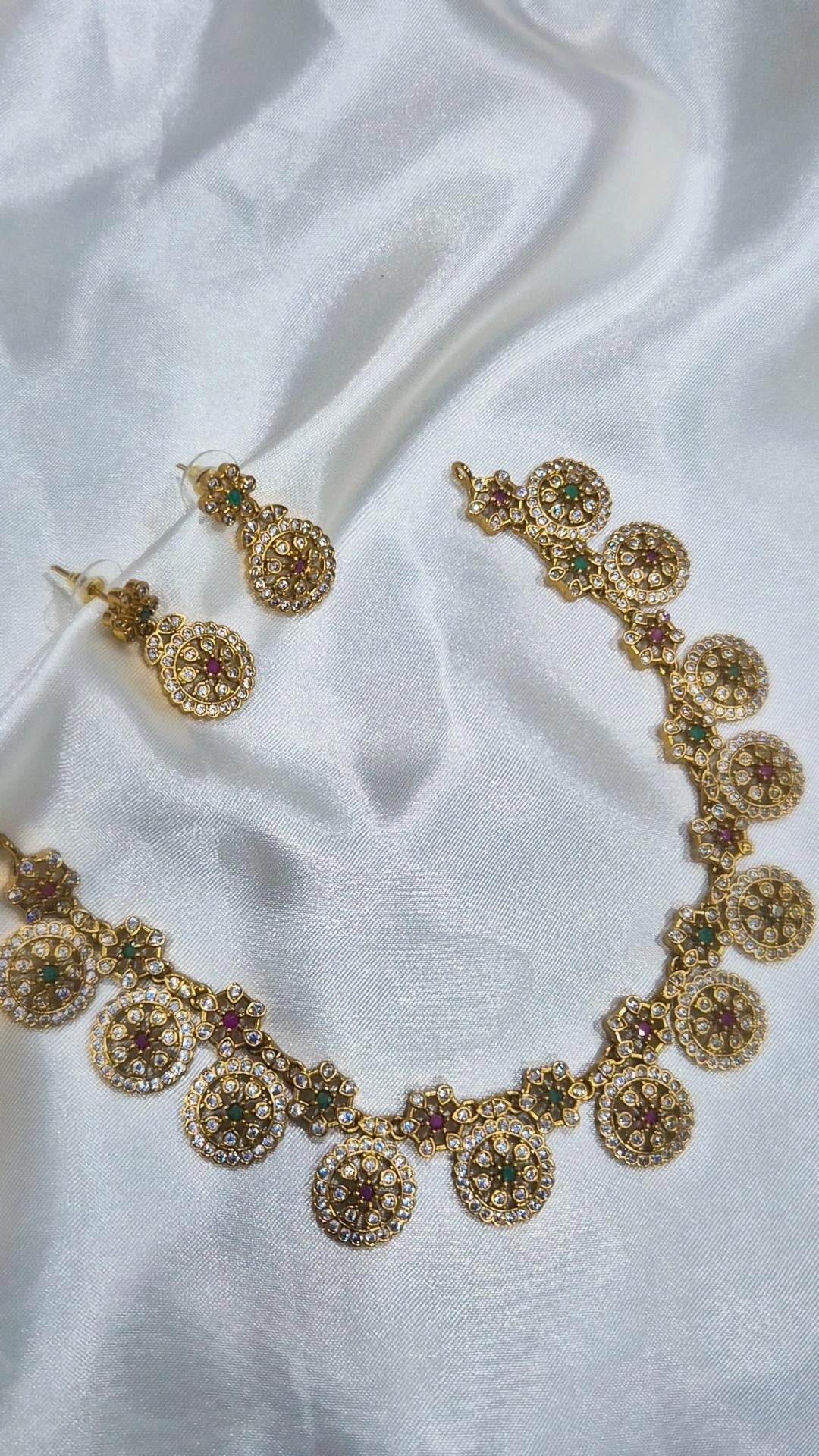 Gold-tone round motif kundan necklace and earring set laid on white fabric