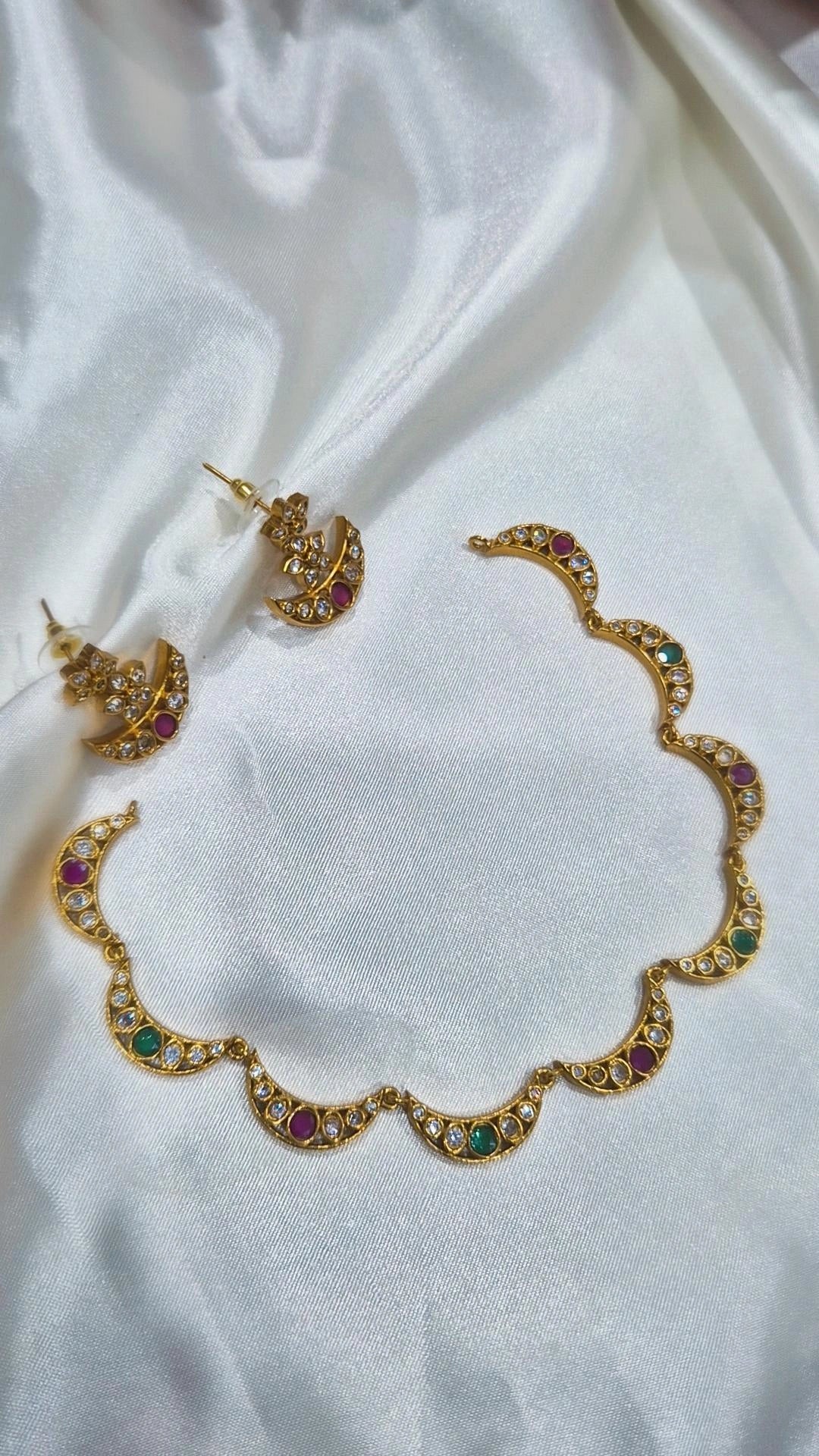 Gold-tone crescent necklace and matching stud earrings with white, ruby, and emerald stones
