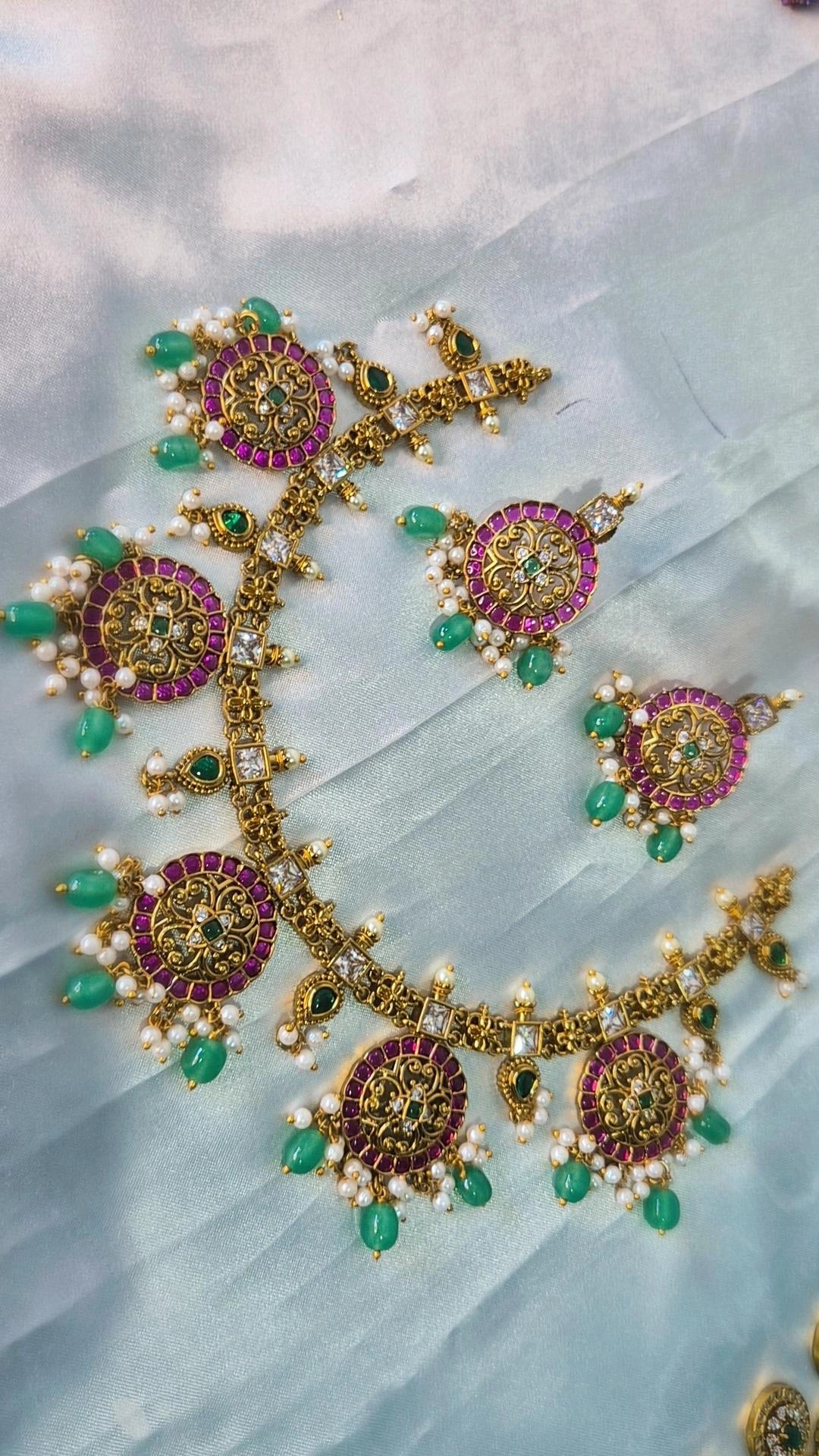 Kemp ruby emerald necklace set with gold filigree medallions, pearl and green bead drops on white fabric