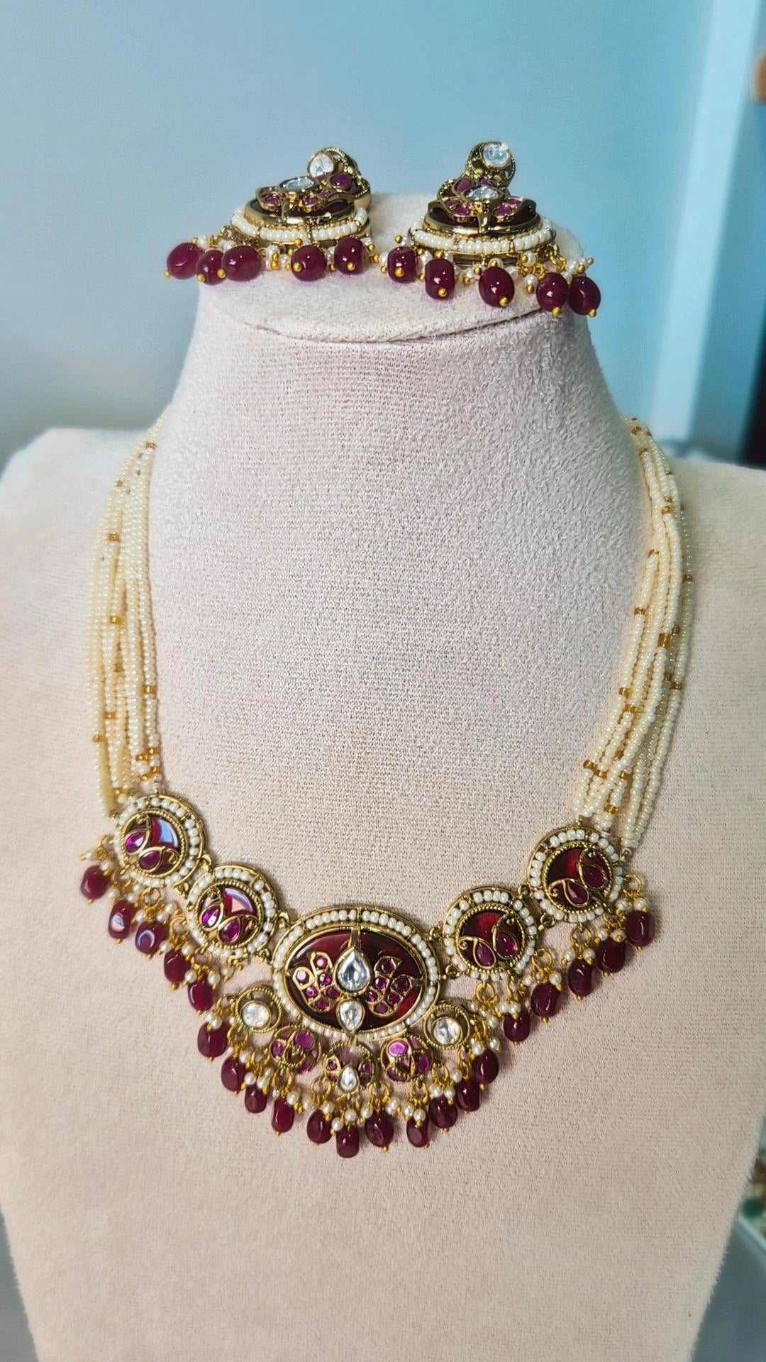 Jadau Kundan ruby necklace with pearl strands and circular medallions displayed on jewellery bust with matching chandbali earrings