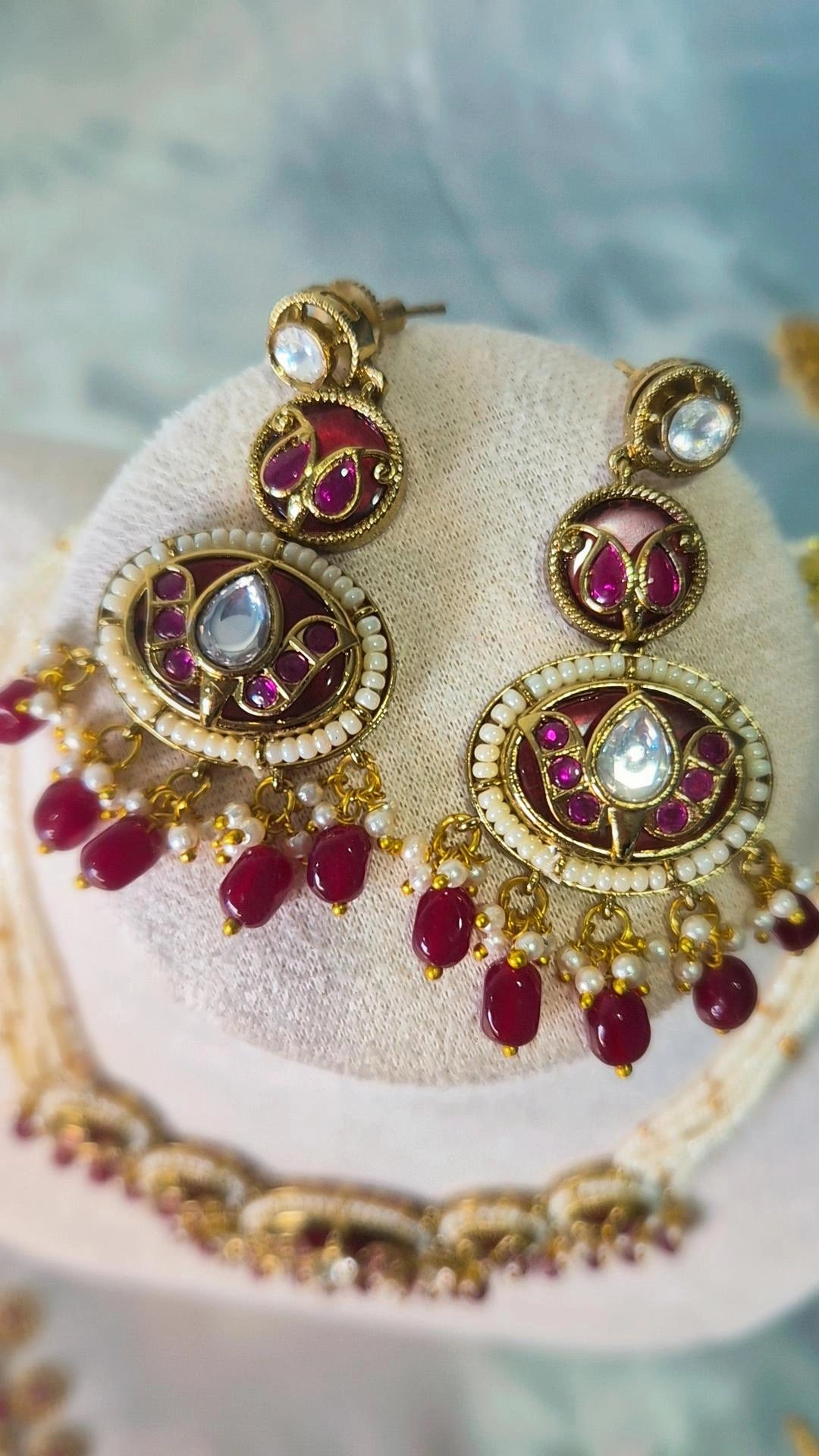 Close-up of Jadau Kundan ruby chandbali earrings with enamel work and ruby bead drops on jewellery stand