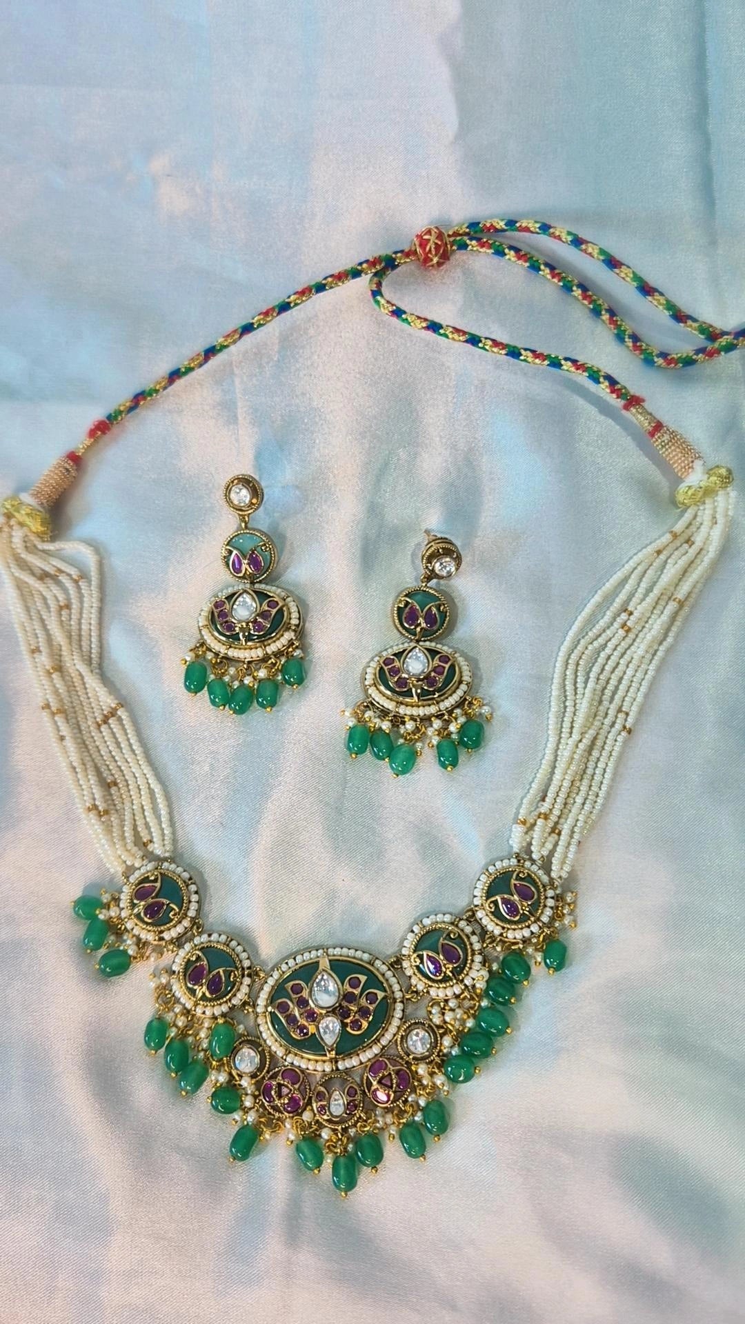 Jadau Kundan emerald green necklace set with pearl strands and chandbali earrings laid flat on white fabric