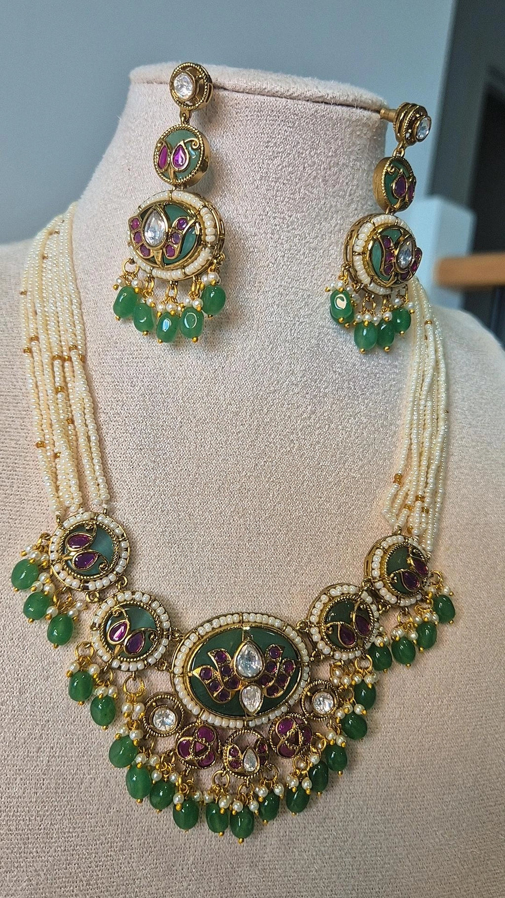 Close-up of Jadau Kundan emerald green necklace with Kundan stone medallions and emerald bead drops on jewellery bust