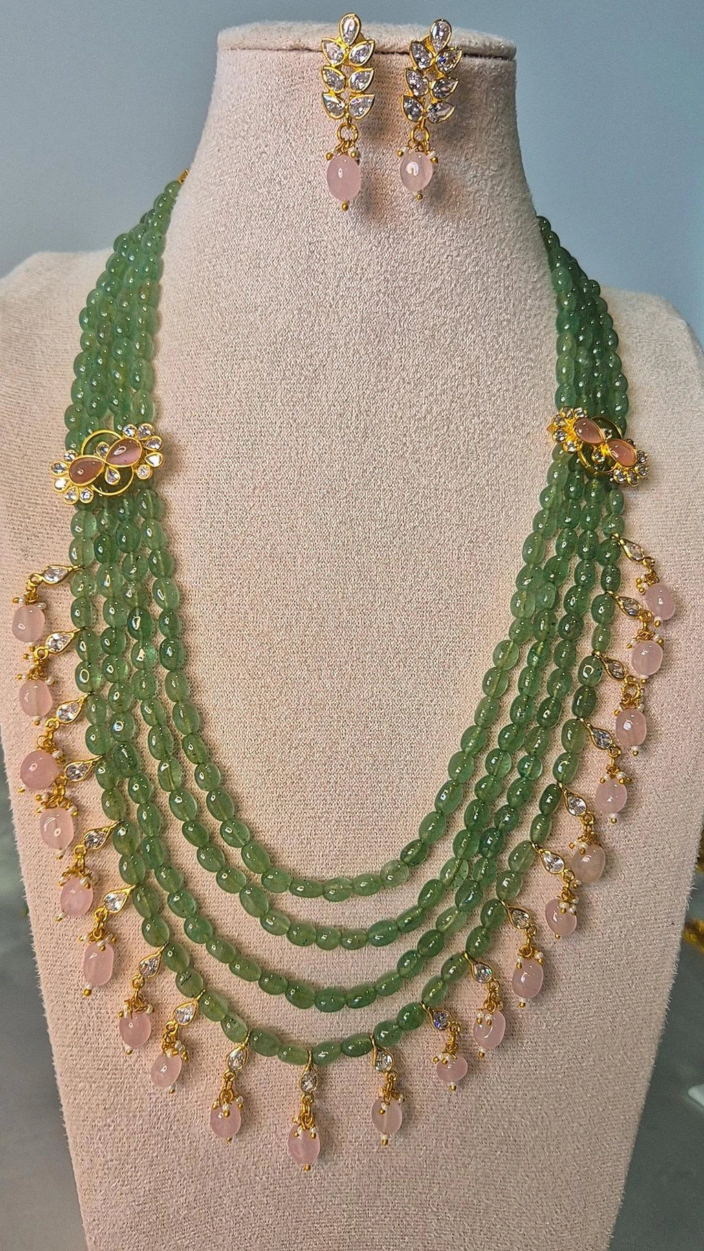 Jadau Kundan emerald green bead long necklace with gold floral connectors and pink rose quartz drops displayed on jewellery stand