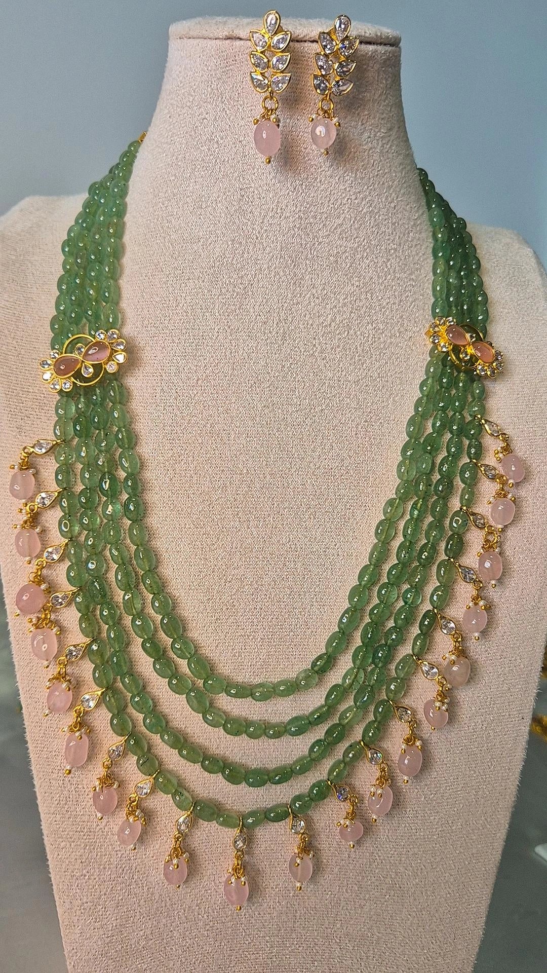 Jadau Kundan emerald green bead long necklace with gold floral connectors and pink rose quartz drops displayed on jewellery stand