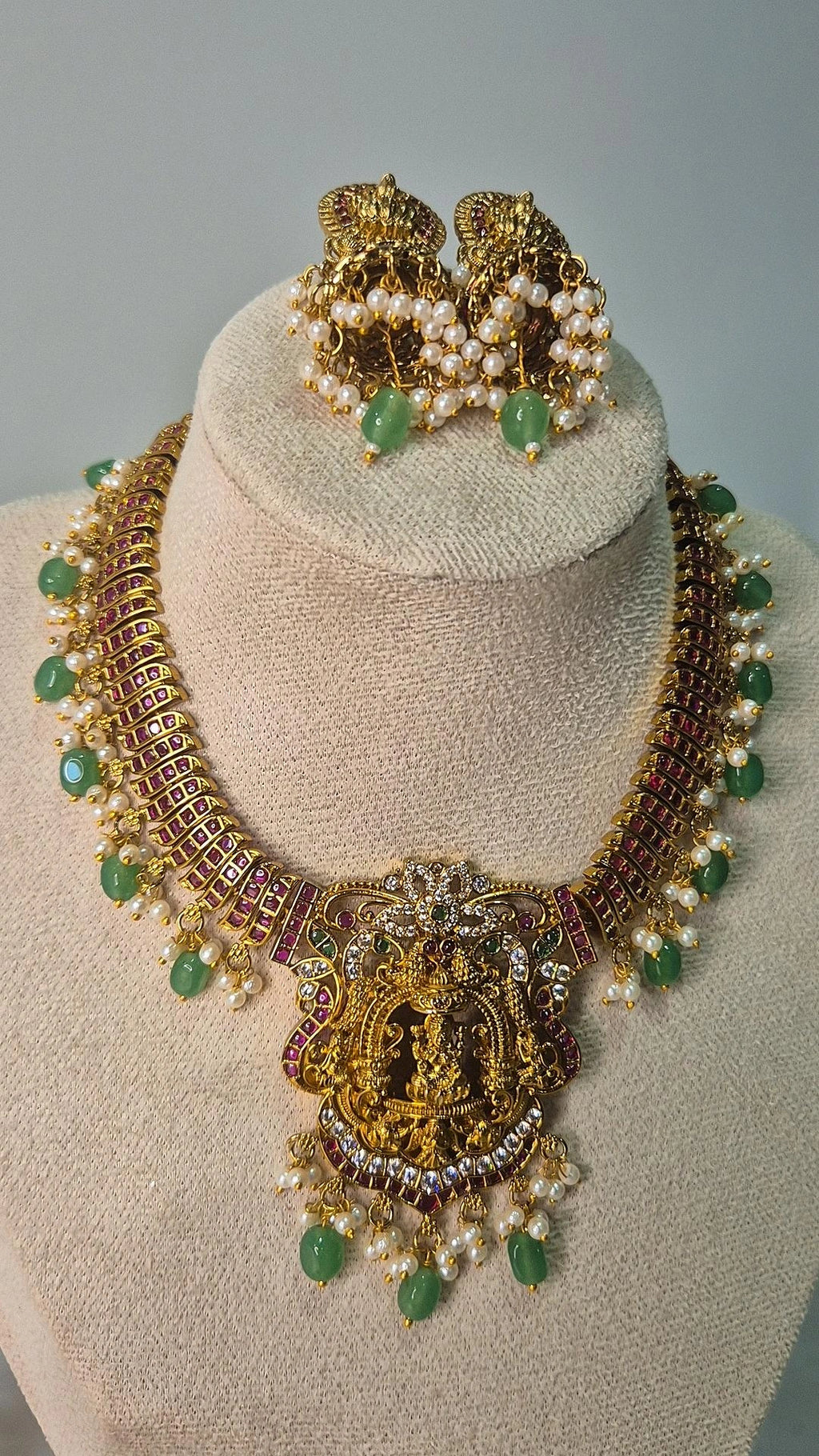 Lakshmi temple jadau choker necklace with ruby chain, pearl drops and emerald beads displayed on jewellery bust with matching jhumka earrings