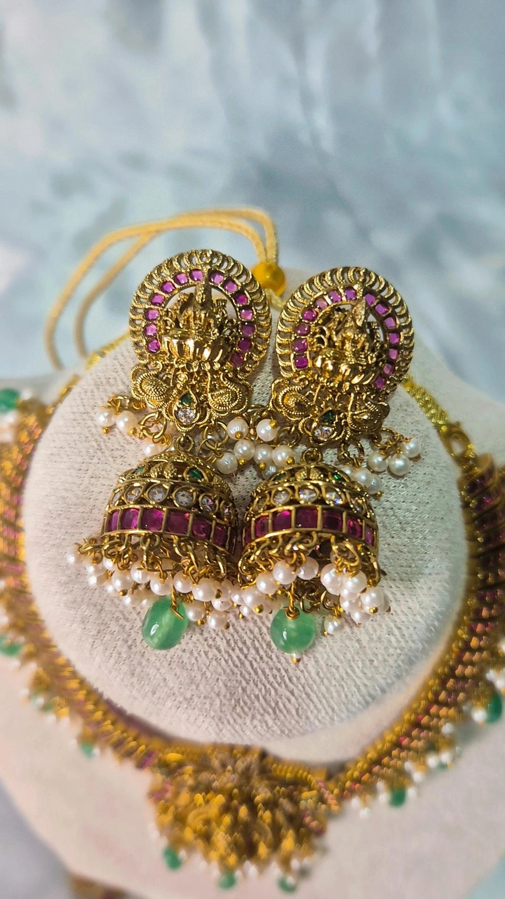 Close-up of ruby Lakshmi jhumka earrings with pearl clusters and emerald bead drops on jewellery stand