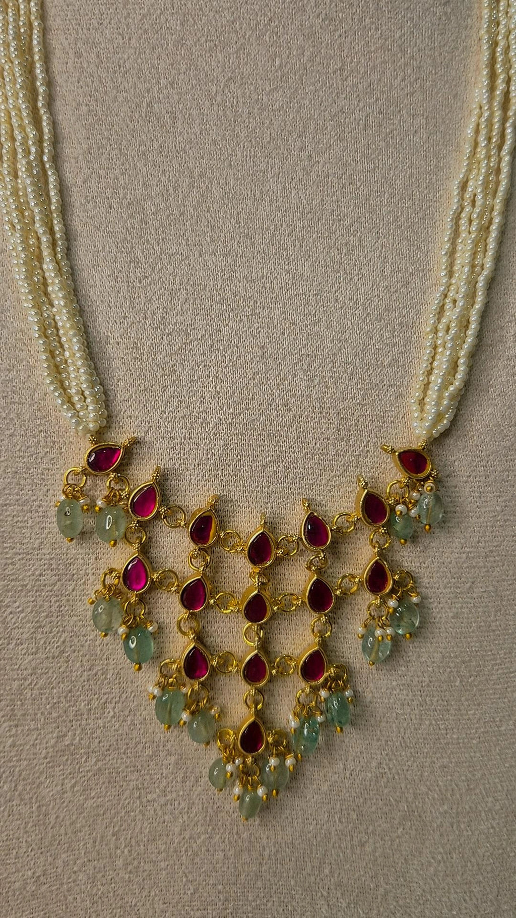 Close-up of Jadau Kundan ruby and emerald waterfall pendant with teardrop stones and pearl accents on pearl strand necklace