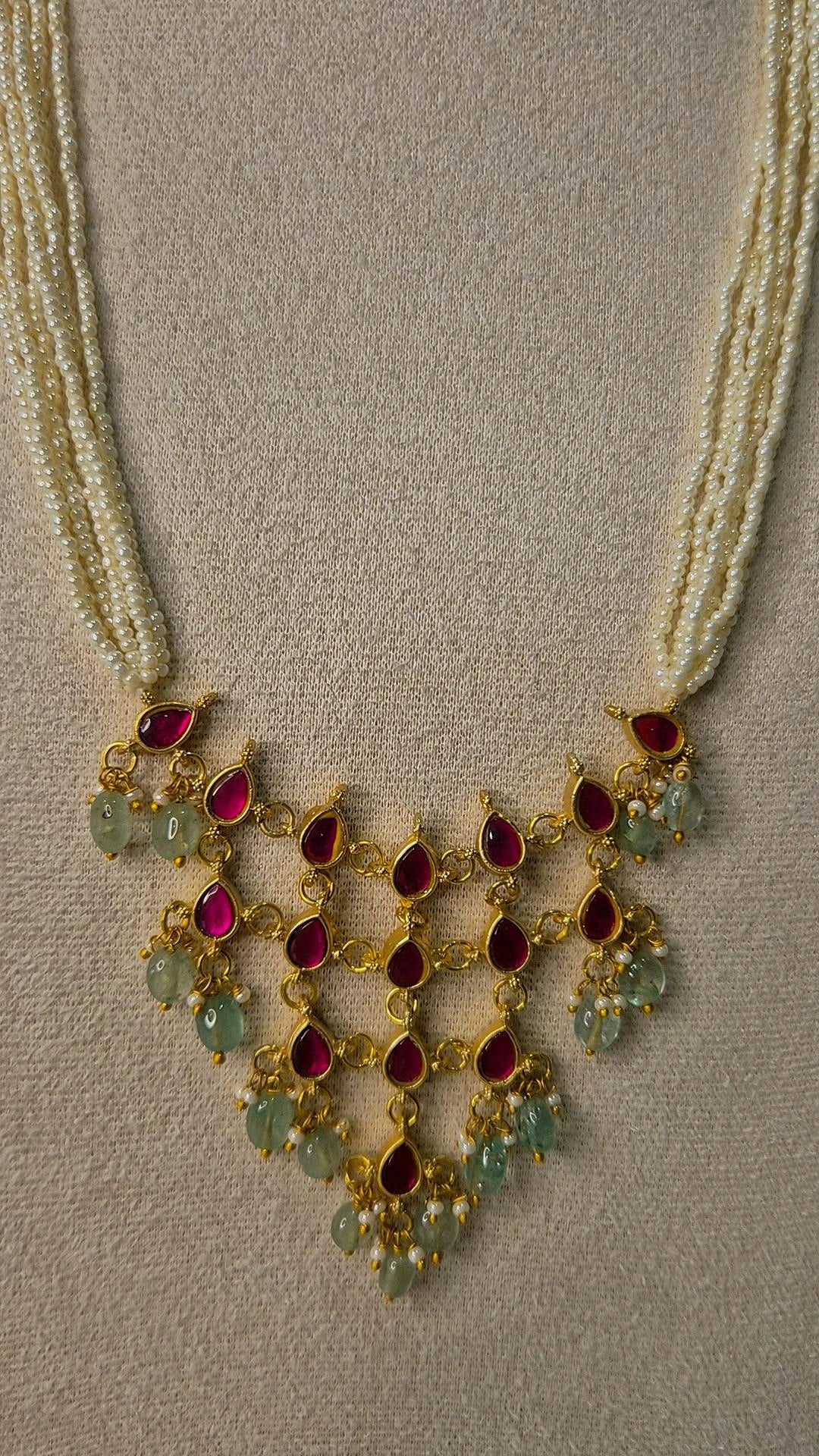 Close-up of Jadau Kundan ruby and emerald waterfall pendant with teardrop stones and pearl accents on pearl strand necklace