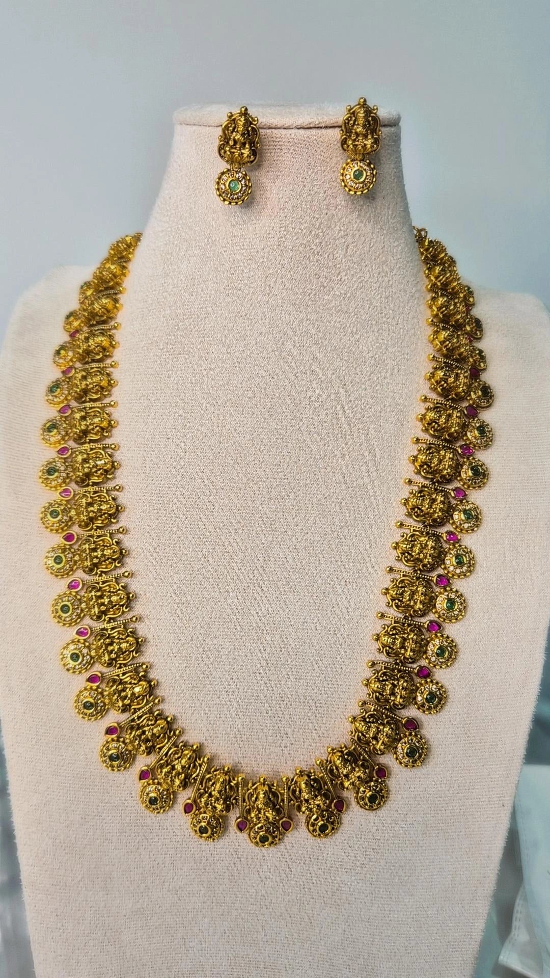 Lakshmi temple antique gold long haram necklace with ruby and emerald accents and matching ball drop earrings on jewellery bust