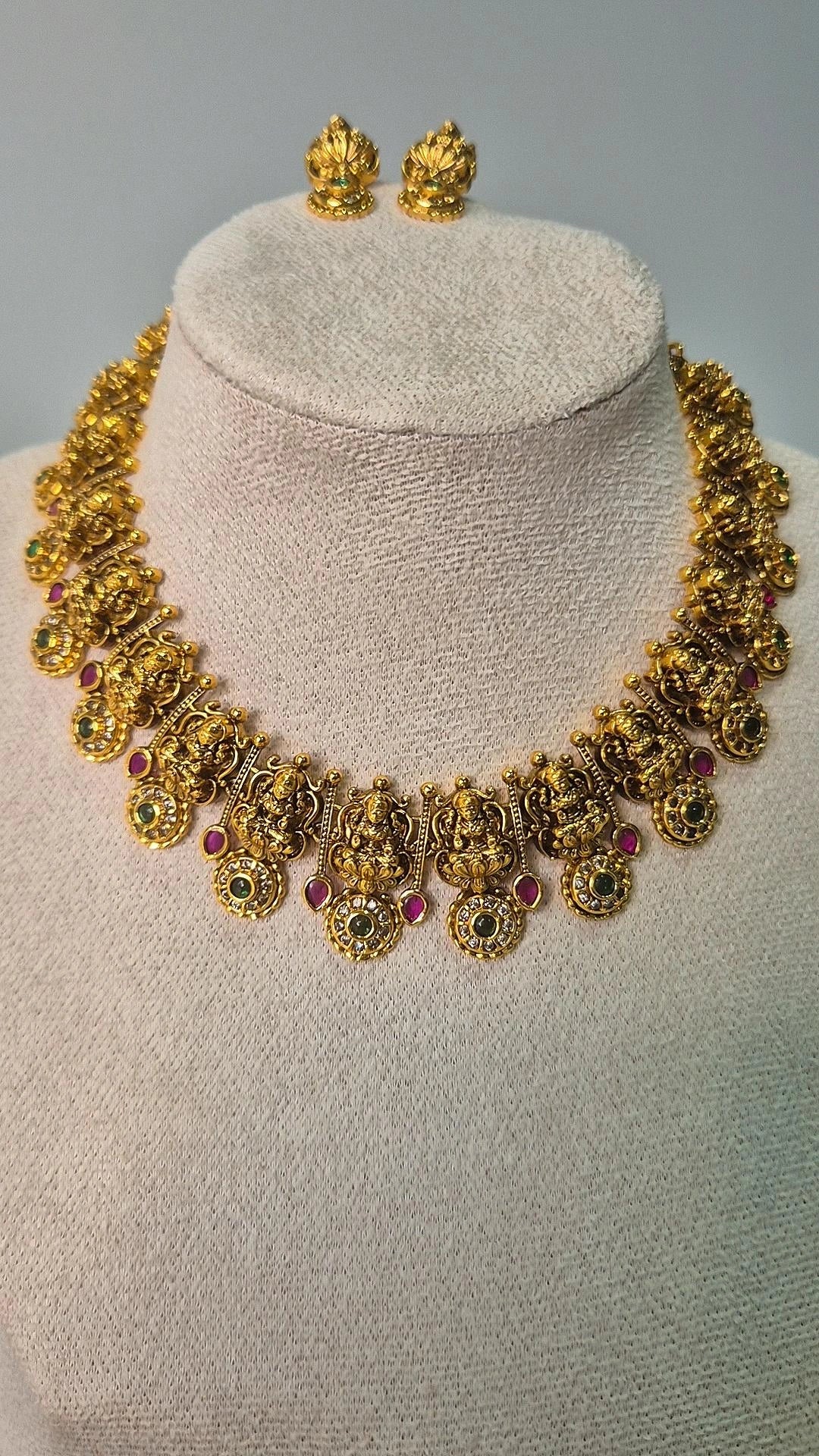 Lakshmi temple antique gold choker necklace with ruby and emerald stone accents and matching Lakshmi stud earrings on jewellery bust