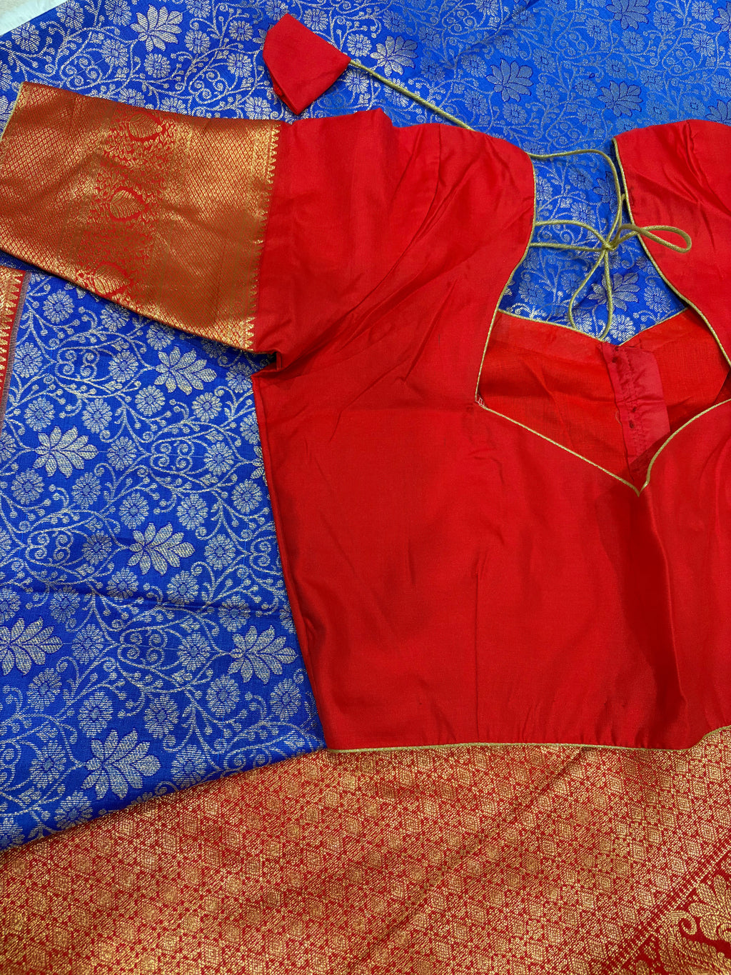 Red boutique stitched blouse with Kanjivaram zari sleeves laid on blue saree - front view