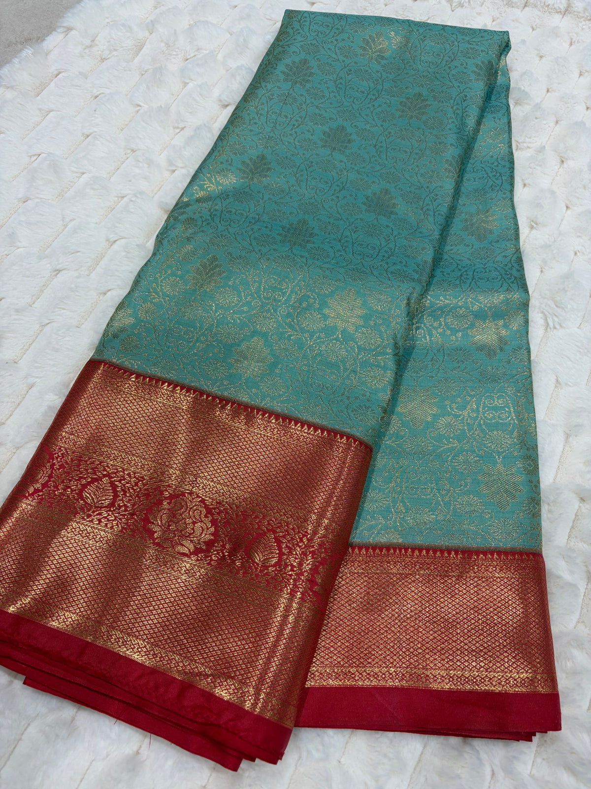 Teal Kanjivaram silk saree folded showing all-over gold zari lotus jaal and deep red border