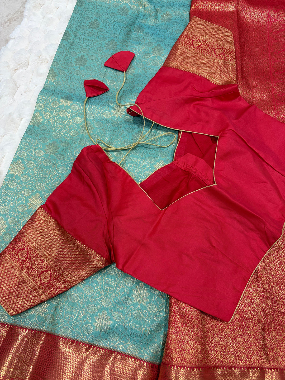 Red boutique stitched blouse with Kanjivaram zari sleeves laid on teal saree - back view with dori ties