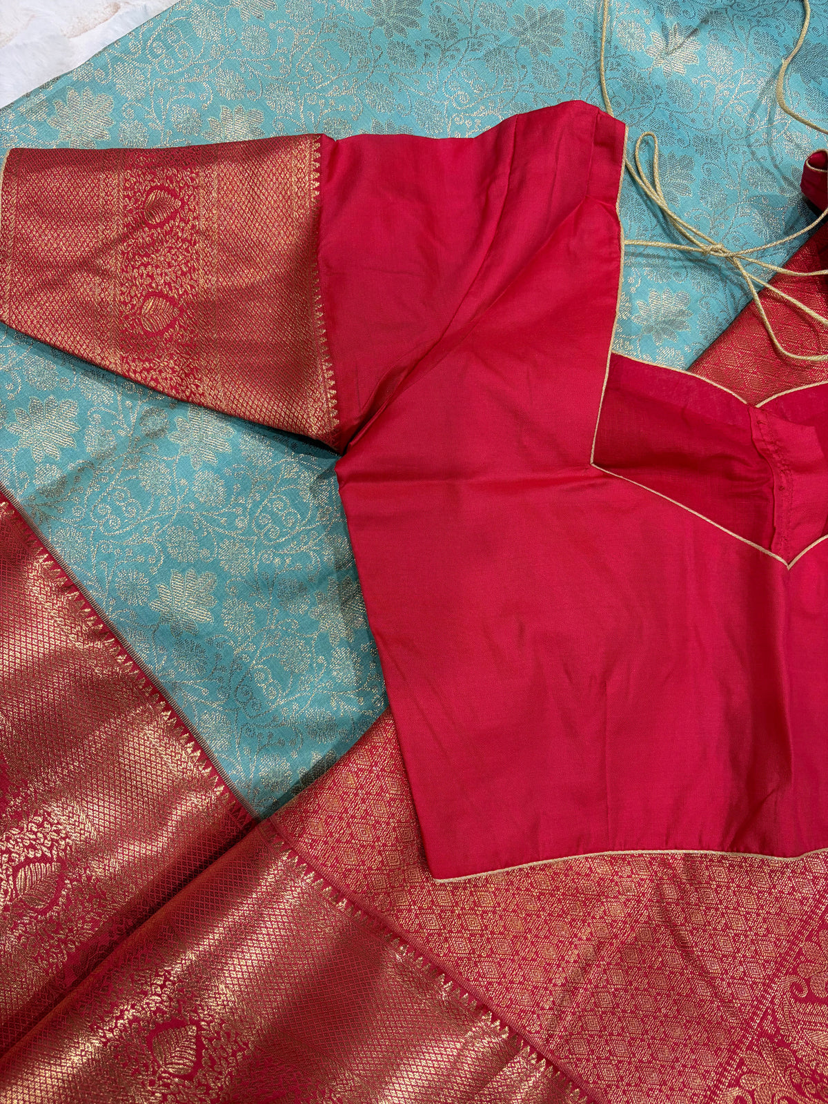Red stitched blouse with sweetheart front neckline and gold piping on teal Kanjivaram saree