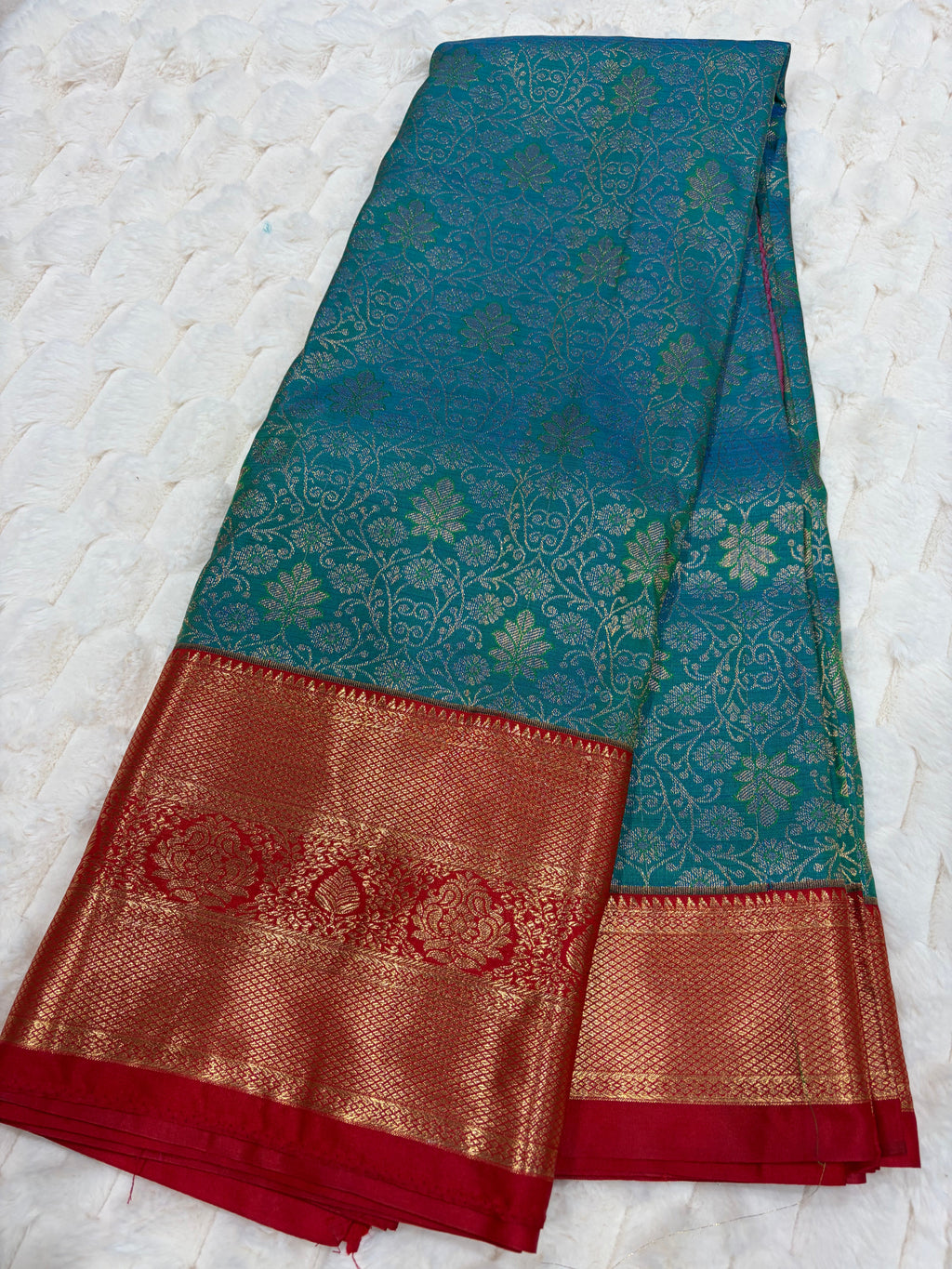 Teal Kanjivaram silk saree folded showing all-over gold zari floral jaal and wide red gold border