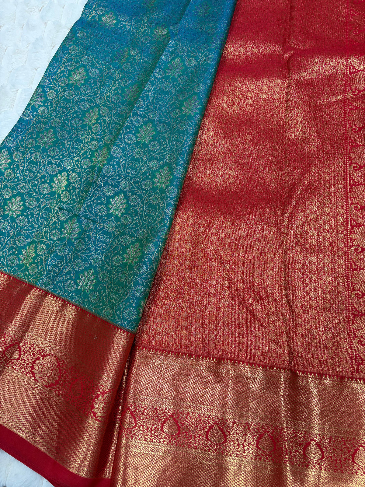 Close up of teal Kanjivaram saree showing gold zari floral pattern and wide red antique gold border