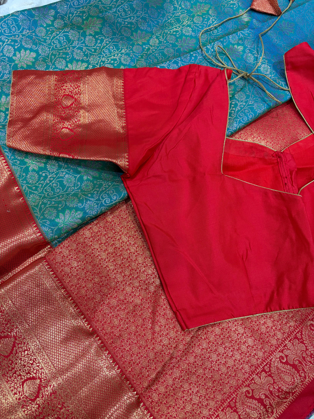 Red boutique stitched blouse with sweetheart back neckline and gold piping on teal Kanjivaram saree