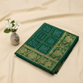 Green Bandhani Kanjivaram saree on cream background with flower vase